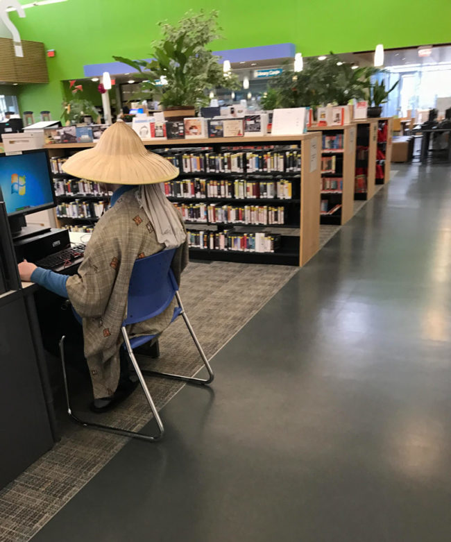 Dude casually wearing an Asian rice hat in a library