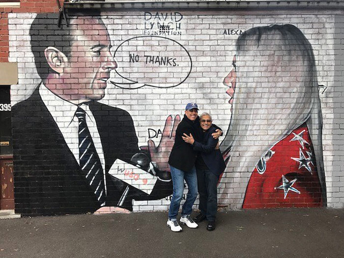 Jerry Seinfeld in front of a mural of himself rejecting Kesha's hug