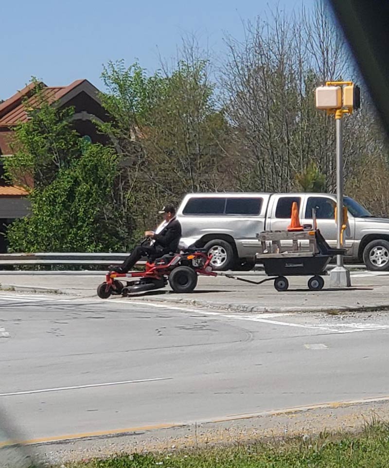 Just a man in a suit driving through the city on his lawn mower