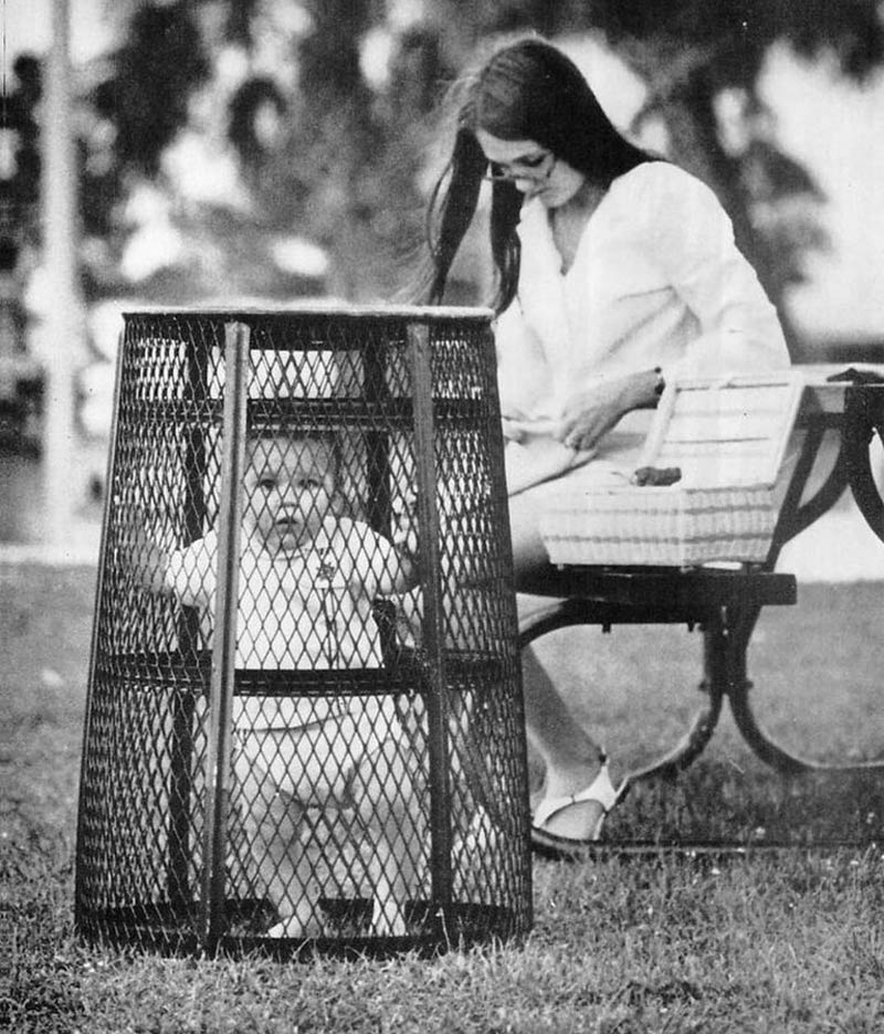 Mom uses a trash can to contain her baby while she crochets in the park, 1969