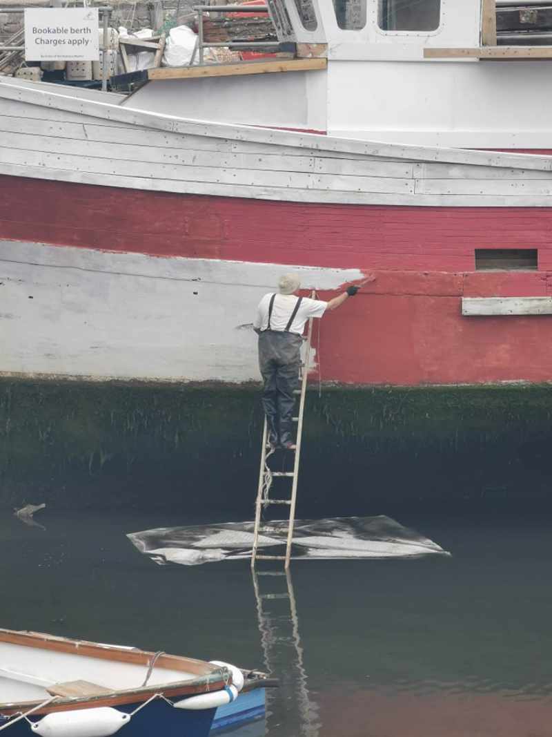 This guy painting his boat with a ladder in the water and a floating dust sheet